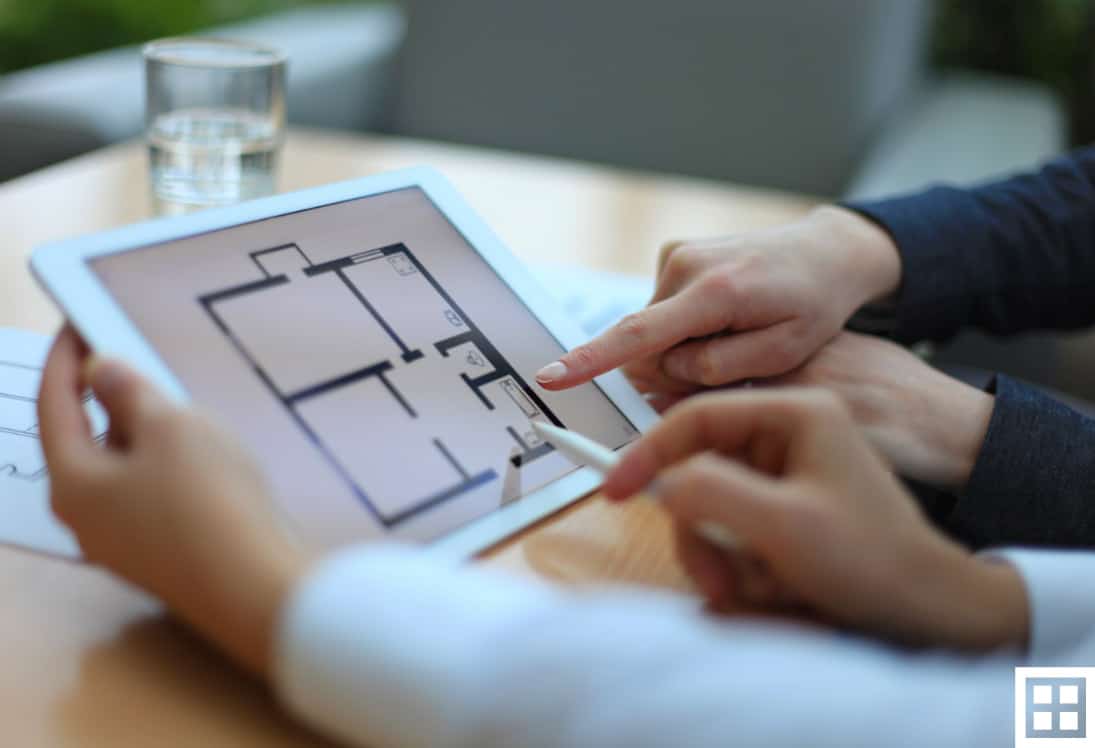 Two people pointing and discussing floor plans displayed on a digital tablet.