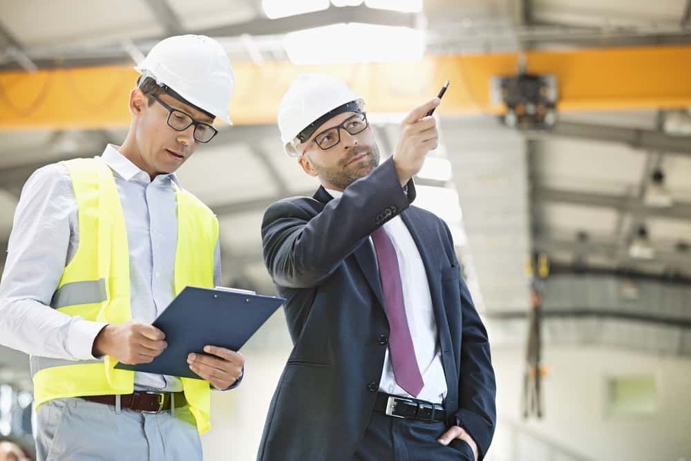 Businessman with supervisor having a discussion in a warehouse wearing hard hats.